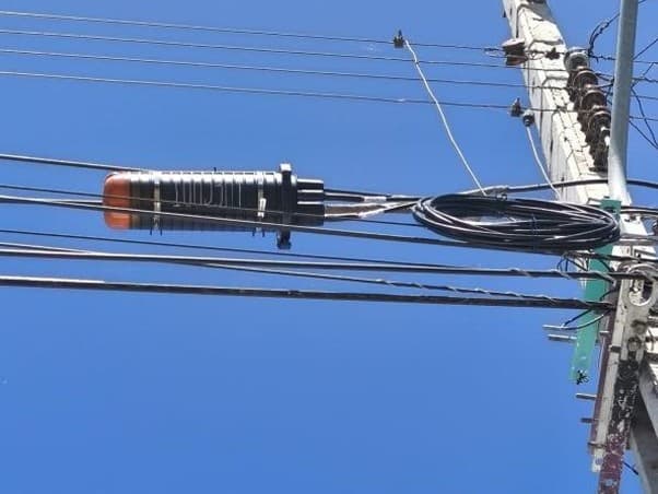 Mufa de empalme y reserva de fibra enrollada en un tendido aéreo junto al poste