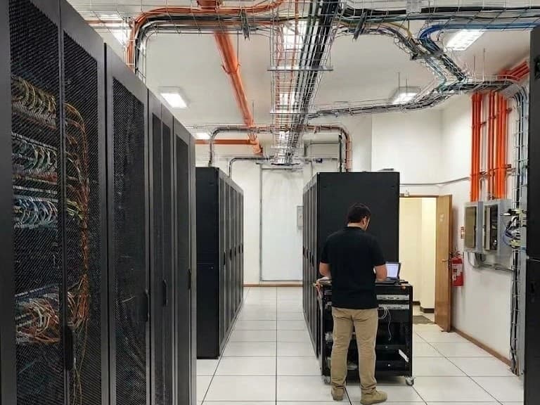 Sala técnica terminada con filas de racks, piso técnico y escalerillas, con un técnico trabajando en un rack móvil