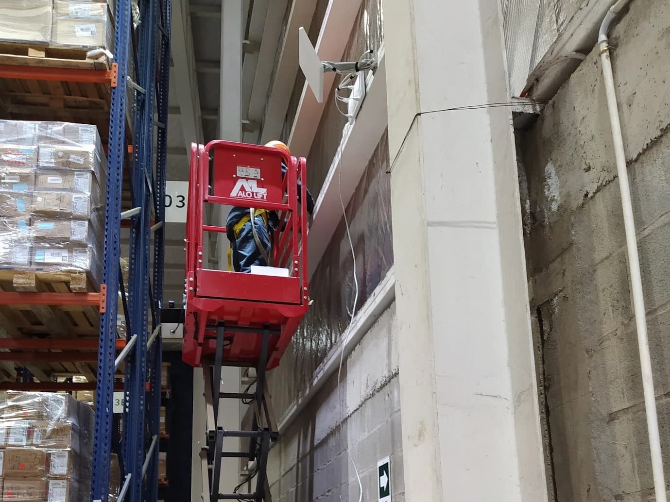 Técnico instalando un punto de acceso en altura en una bodega, desde un elevador