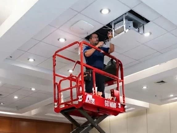 Técnico en un elevador tijera instalando en el cielo de un salón de eventos, con un punto de acceso a la vista