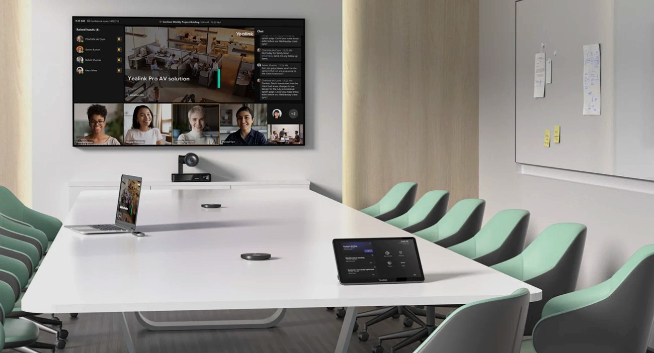 Sala de reuniones con la pantalla al centro del muro, la cámara bajo ella y micrófonos y panel de control sobre la mesa